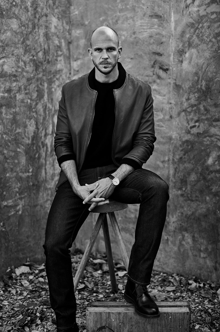 Gustaf Skarsgard posing in a black and white photo while sitting on a stool.