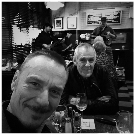 Ian Gelder and Ben Daniels inside a restaurant sharing wine.