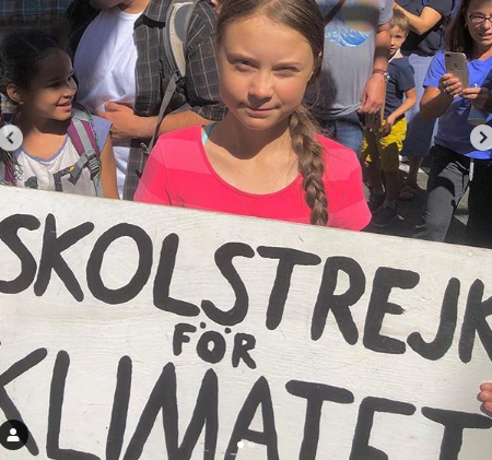 Greta holding a placard which reads "skolstrejk för klimatet" which translates to School strike for climate.