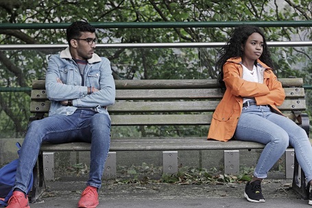 A guy looking at a girl at the other end of the bench they are sitting on. Girl is looking away from the guy.