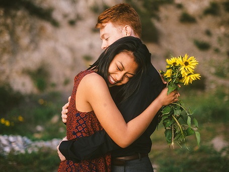 A girl hugging a boy with sunflowers in her hand.