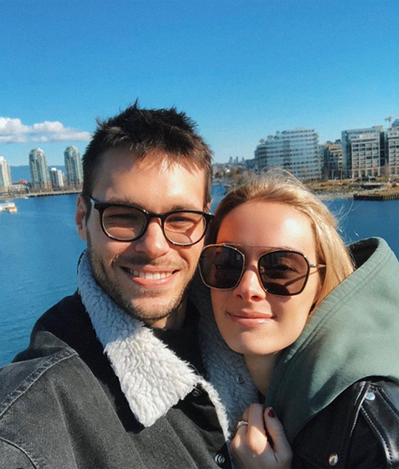 Rachel Skarsten and Alexandre Robicquet taking a selfie near the ocean.