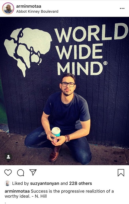 Armin Mota's photo sitting down in front of a wall with the words written, World Wide Mind'.