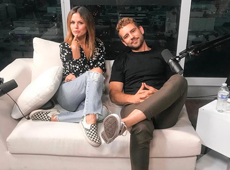 Rachel Bilson and Nick Viall sitting on a sofa with a mic in front of him.