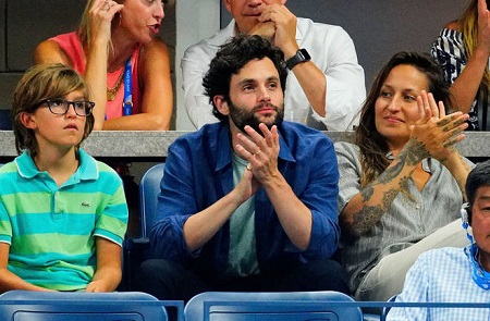 Domino Kirke and Penn Badgley clapping with Cassius beside him during a game.