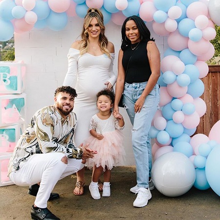 Cory Wharton sitting in his daughter's height who is smiling hardly, as Taylor stands with her hand in her belly besides Cheyenne Floyd.