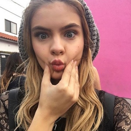 Brighton Sharbino pinching on either side of her cheeks with one hand, making pout lips.