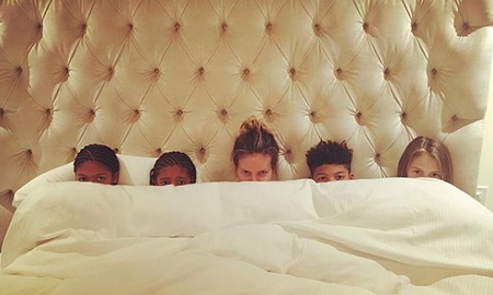 Heidi Klum in the center in bed covered by quilt upto the mouth level with her four kids. (two on either side)