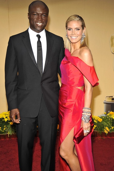 Heidi Klum in red and Seal in a tuxedo posing with a smile.