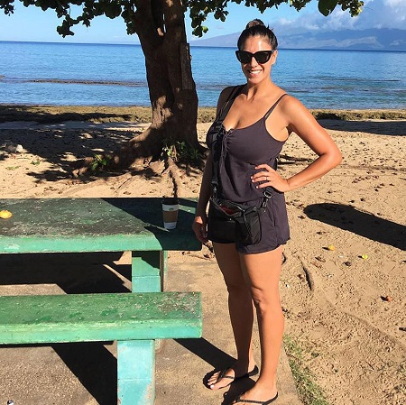 Christina Mauser stands by a beach bench and smiles with her one hand in her waist.