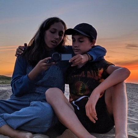 The son and daughter of Dolly Wells and husband Mischa Richter arm in arm watching a camcorder.