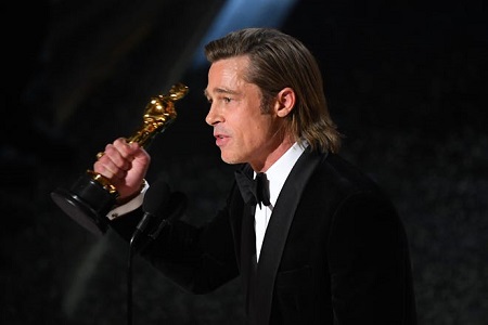 Brad Pitt raising an Oscar in his right hand in front of the mic during the acceptance speech..