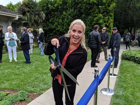 Cara Kokenes taking a huge scissor about to cut a blue ribbon.