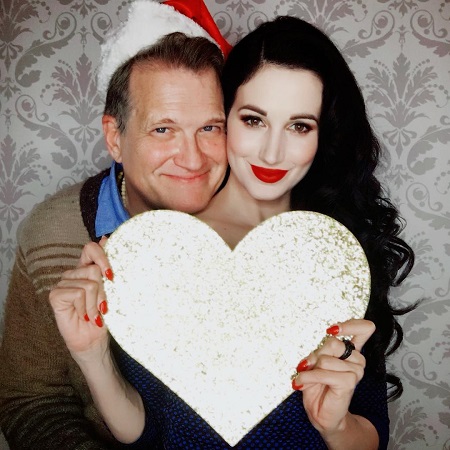 Harwick holding a huge silver heart as Carey hugs her from behind.