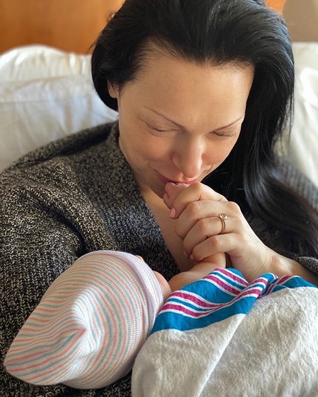 Laura Prepon kissing her baby's hand in a hospital bed.