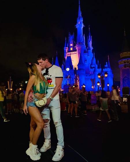 Juliette Porter kissing her boyfriend Sam Logan in front of a Disney castle in the evening.